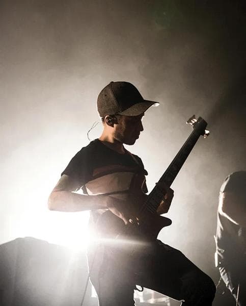 Lamood guitar lifestyle - Bass guitarist wearing a Lamood baseball cap performing on stage under bright spotlight and hazy atmospheric lighting.