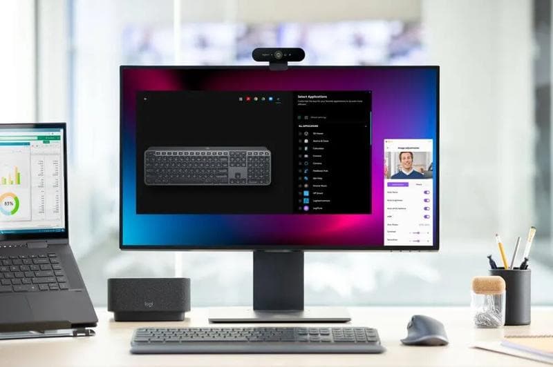 desk featuring logitech products setup professional - Computer setup with monitor, webcam, wireless keyboard, mouse, and docking station on a wooden desk.