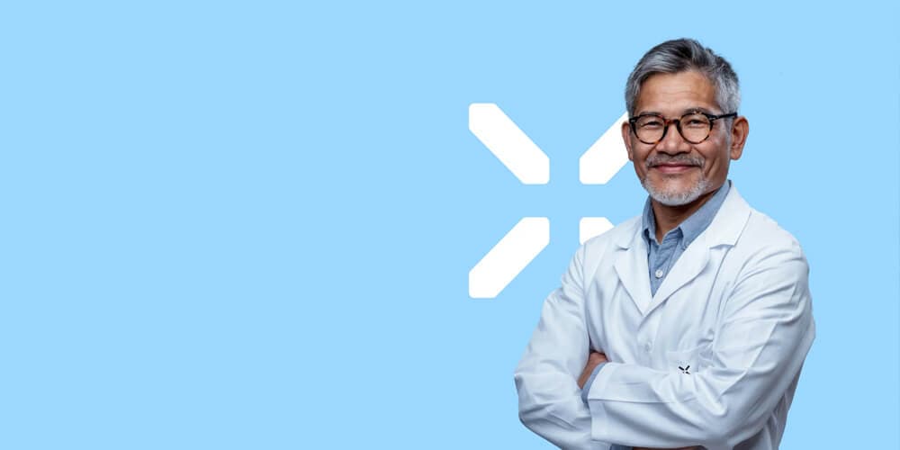 Smiling male doctor in a white lab coat standing against a light blue background with the PlexusDx logo.
