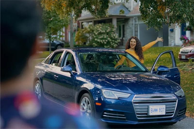 appy woman standing by a blue Audi sedan in a residential neighborhood, representing a Kijiji car sale.