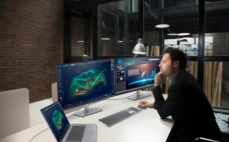 Professional male analyzing 3D terrain data on dual Dell UltraSharp monitors in a modern office.