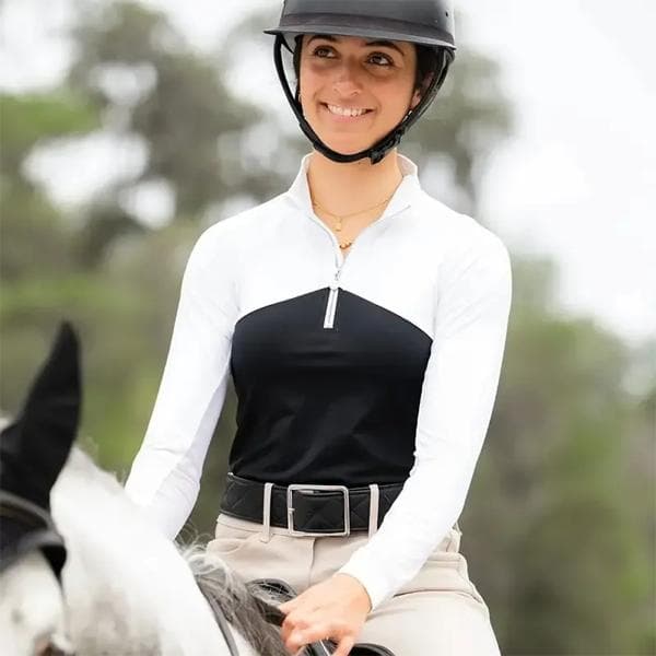 Woman on horse - Smiling equestrian rider wearing a black and white quarter-zip sun shirt and safety helmet.
